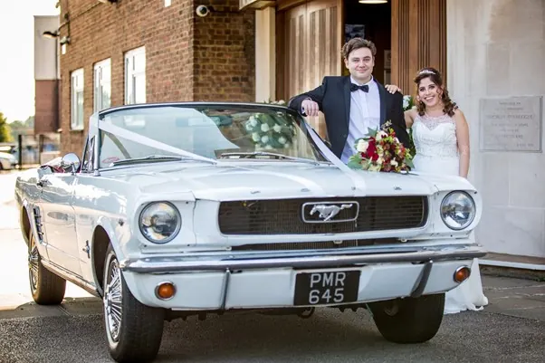 The bride and groom with a classic white Mustang convertible